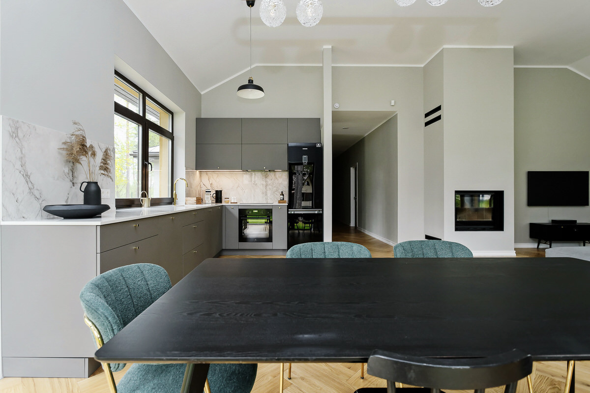 Zaļas krāsas virtuves krēsli, tumšās krāsas galds, virtuves mēbeles ar olīvkrāsas fasādēm un zelta krāsas aksesuāriem.