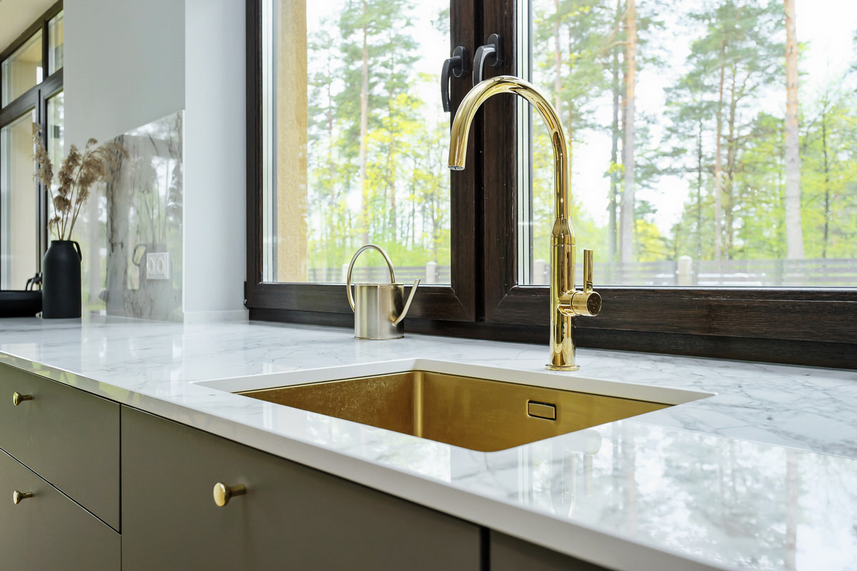 Akmens galda virsma, elegants zelta krāsas izlietnes krāns, kas piešķir virtuvei ekskluzīvu izskatu